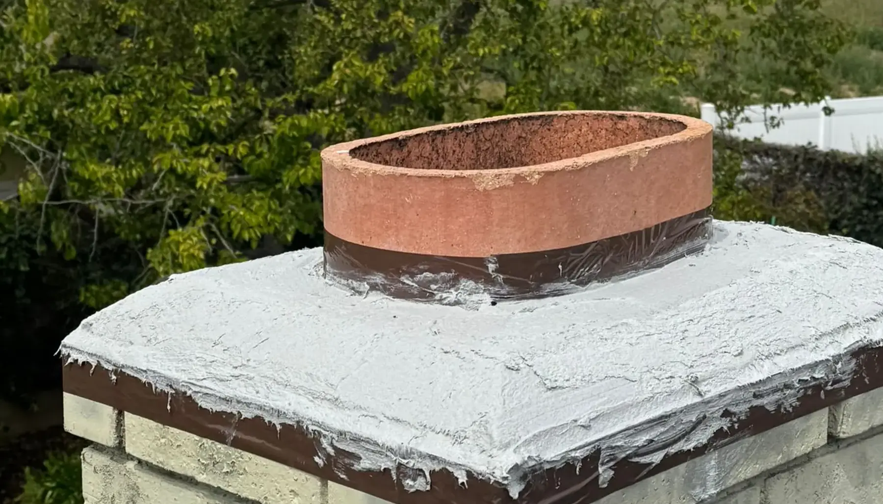 Chimney crown with a fresh protective coat, seen from the roof with trees behind
